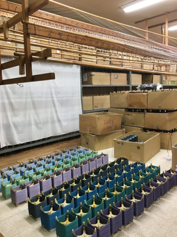 床に並べられた糸枠。一本一本糸を上に引き上げて穴に通します。