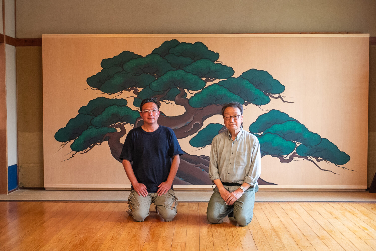 保存会会員手作りの老松鏡板を背景に嶋さん(左)と戸田さん(右)