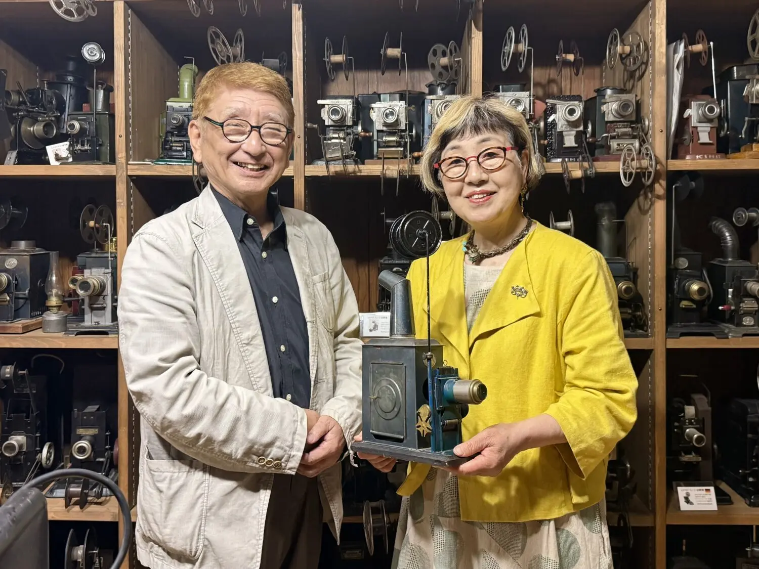 国内外の玩具映写機の前に並ぶ太田さんご夫妻